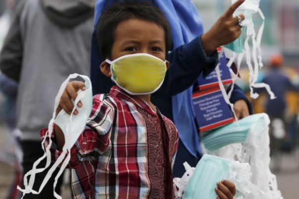 A child offers face masks to people along a haze shrouded street in Palembang, on the Indonesian island of Sumatra, September 20, 2015. Indonesia will take 30 days to bring smouldering forest fires under control, the national disaster management agency said on Friday, as smog from the fires pushes pollution in Southeast Asia to record highs. REUTERS/Beawiharta